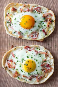 two pizzas with eggs on them sitting on top of a table next to each other