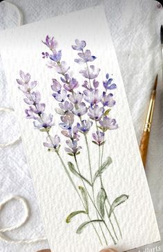 watercolor painting of lavender flowers on white paper next to crochet hooks and yarn