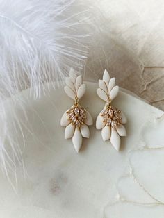 two pairs of white and gold earrings with crystals on them, sitting next to feathers