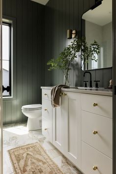 a bathroom with green walls, white cabinets and a rug on the floor in front of the sink