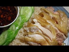 a plate with rice, cucumber and meat on it next to a bowl of sauce