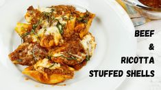 a white plate topped with stuffed shells covered in sauce next to a bowl of pasta