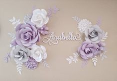 there are paper flowers on the wall with name spelled in white and lilac colors