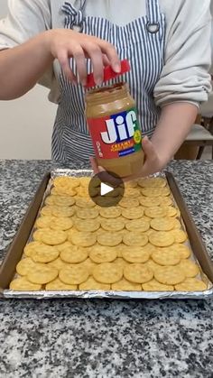 a woman in an apron is spreading peanut butter on cookies