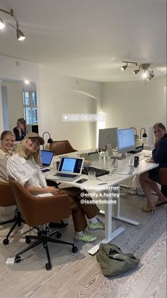 a group of people sitting around a table with laptops and monitors on it in an office