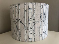 a white lamp shade with black and white trees printed on the fabric, sitting on a table