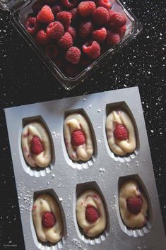 some raspberries are in the middle of a muffin tin with icing