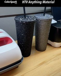 two black and white cups sitting next to each other on a wooden table near a laptop