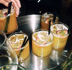 there are four glasses with drinks in them on the tray and one is filled with ice