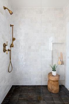 a white tiled bathroom with a wooden stool and shower head