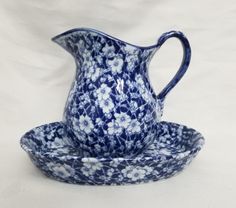 a blue and white flowered pitcher on a saucer with a matching plate in the shape of a bowl