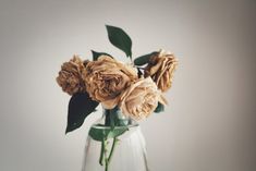 a glass vase filled with flowers on top of a wooden table next to a white wall