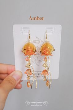 a pair of orange earrings is being held in front of a white card with the word amber on it