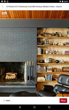 an eames lounge chair and ottoman in front of a fireplace with bookshelves