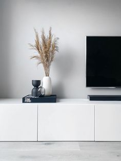 a white entertainment center with a flat screen tv on it's stand and some vases