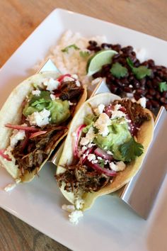 three tacos on a plate with beans and guacamole