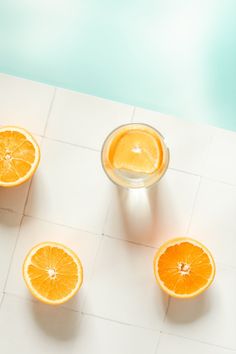 four oranges are placed on a white tile floor next to a glass of water