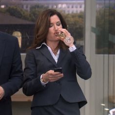 a woman in a business suit drinking from a wine glass and looking at her cell phone