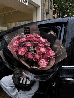 a bouquet of pink roses sitting in the back of a black car with its door open