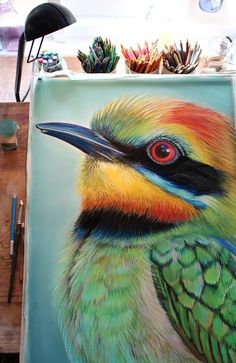 a painting of a colorful bird on a table with pencils and paintbrushes