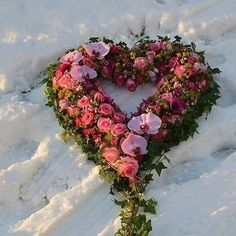 a heart shaped wreath with pink flowers in the middle of it on snow covered ground