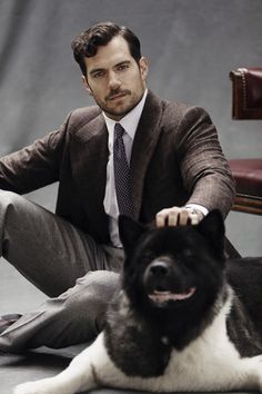 a man in a suit sitting next to a black and white dog on the floor