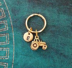 a gold keychain with a tractor and initial charm hanging from it's side