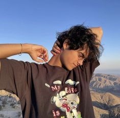 a person standing on top of a mountain with their hands behind his head and wearing a shirt that says my life is cruel