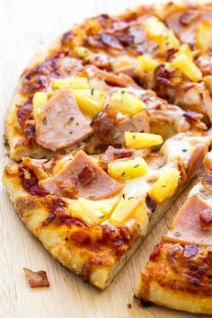 a pizza with pineapple and ham on it sitting on a cutting board next to a slice missing