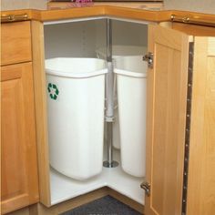 two trash cans sitting in the corner of a kitchen cabinet with their lids down and one is open