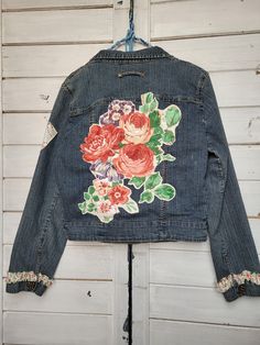 an old jean jacket with flowers on it hanging from a hook in front of a white wall