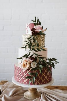 a three tiered cake decorated with flowers and greenery on a wooden table next to a brick wall