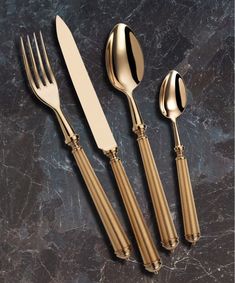 three forks, two spoons and one knife on a marble counter top with gold trim