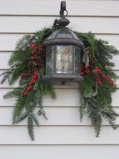 a christmas wreath hanging from the side of a house with pine cones and red berries