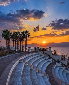 the sun is setting behind some palm trees and an empty stage with people sitting on it