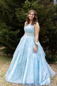 a woman wearing a blue dress standing in front of some trees and smiling at the camera