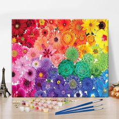 an art work with colorful flowers and paintbrushes on the table next to it