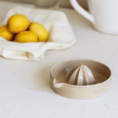 some lemons are sitting on a table next to a white bowl with a strainer in it