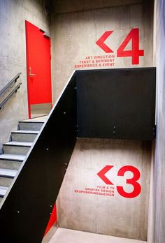 the stairs lead up to an art direction sign and red door with numbers on it