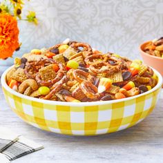 a yellow and white bowl filled with candy cornflakes, pretzels, and cereal