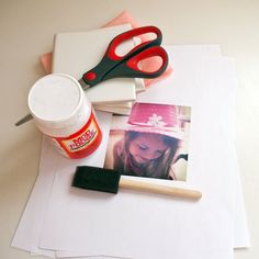 a white table topped with pictures and crafting supplies next to a cup of paint