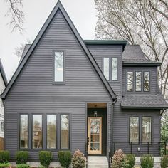 a gray house with lots of windows and bushes in front of the entrance to it