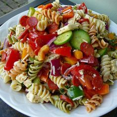 pasta salad with tomatoes, cucumbers, red onions and other vegetables on a white plate