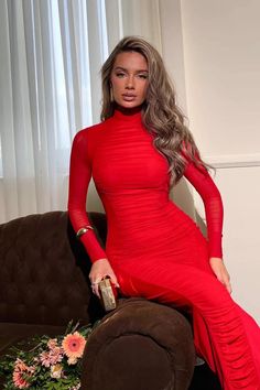 a woman in a red dress is sitting on a brown couch and posing for the camera