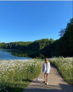 a woman walking down a path next to a lake with wildflowers on both sides