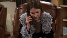 a woman sitting in a chair talking on a cell phone while wearing a fur collar