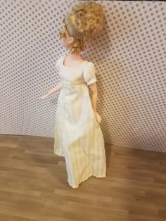 a doll is standing next to a wall with a white dress on it's head