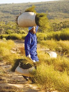 a man walking down a dirt road carrying two bags on his head and another bag over his head