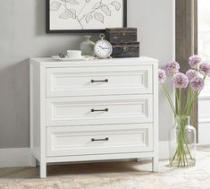 a white dresser with three drawers and two vases filled with flowers on top of it