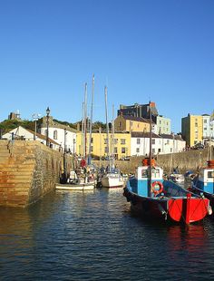 several boats are docked in the water near some buildings and cliffs on a sunny day